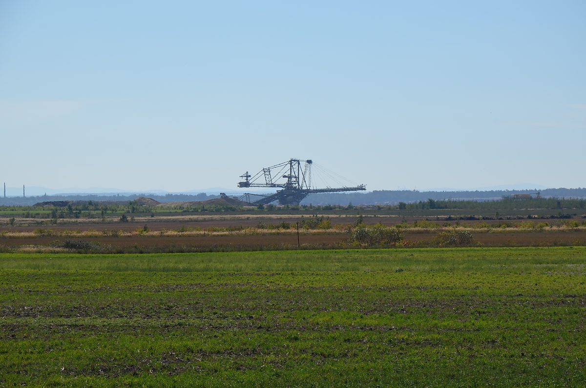 Schaufelradbagger im Braunkohletagebau hinter landwirtschaftlicher Fläche